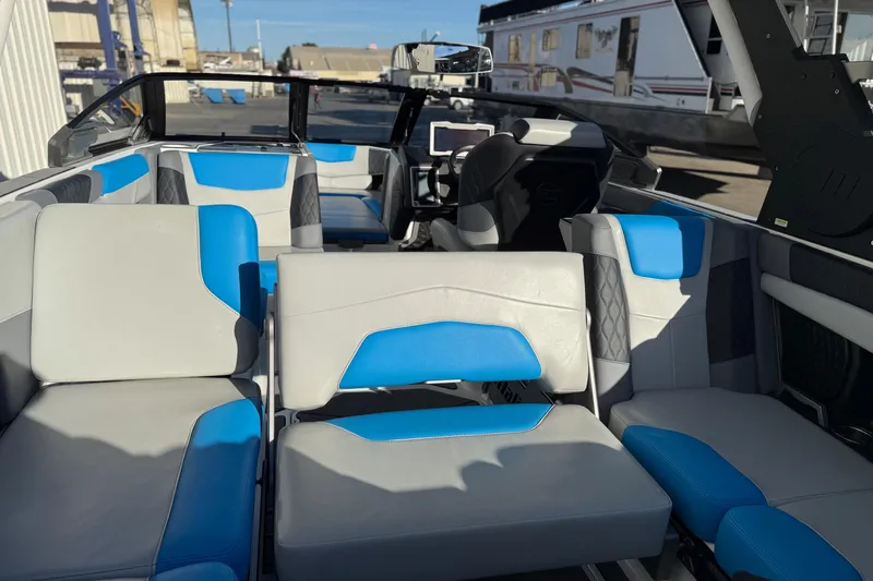 Slide: The Image of 2023 Malibu M240 boat interior with blue and gray seating, docked outdoors. - 26