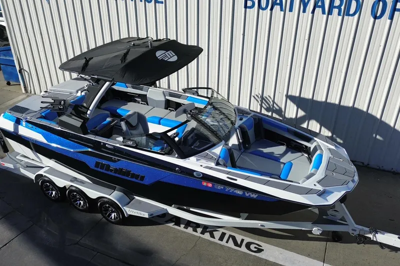 Slide: The Image of 2023 Malibu M240 boat with blue accents on a trailer, parked by a boathouse. - 3