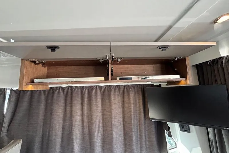 Slide: The Image of 2023 Beneteau Antares 11 interior with open overhead cabinet and mounted TV. - 19