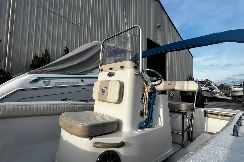 Slide: The Image of 2016 Carolina Skiff EV218 Sea Skiff docked near a covered boat, showcasing helm and seating. - 10