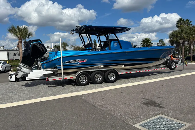 Slide: The Image of 2024 GSX 36 boat on trailer, blue exterior, parked outdoors under cloudy sky. - 1