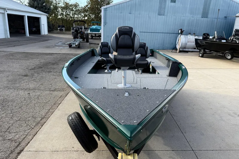 Slide: The Image of 2026 Lund 1700 Explorer Tiller boat, green exterior, parked outdoors near a blue building. - 2