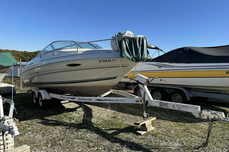 The Image of 2000 Sea Ray 215 Express Cruiser on trailer, parked outdoors under clear blue sky. - 0