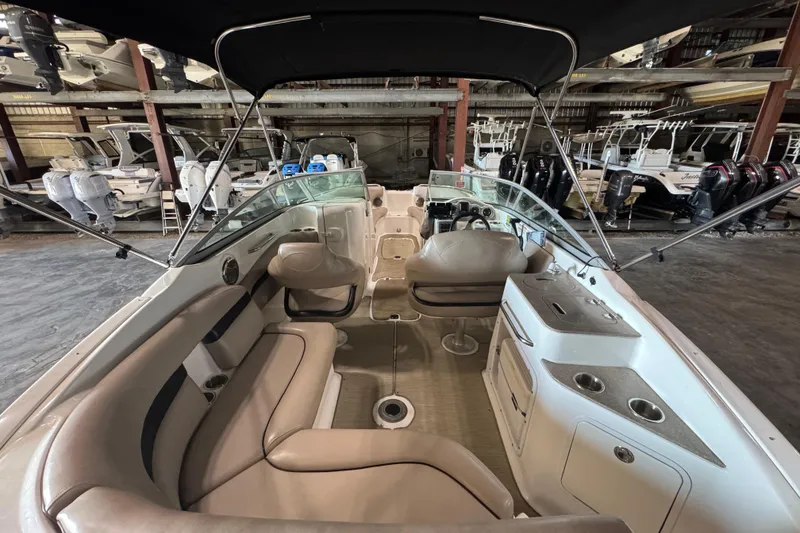 Slide: The Image of 2014 Hurricane SunDeck 2400 OB interior with seating and helm, stored in a boat warehouse. - 11