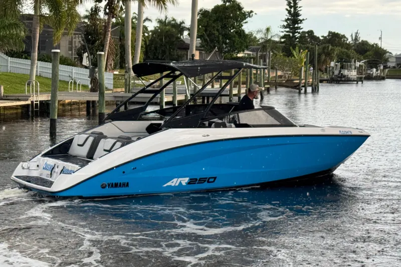 Slide: The Image of 2023 Yamaha AR250 boat cruising on a calm waterway, featuring sleek blue and white design. - 2