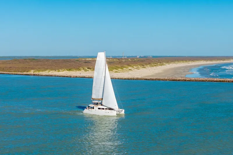 Slide: The Image of Sailing catamaran Lagoon 450, 2013 model, cruising near a sandy coastline under clear blue skies. - 151