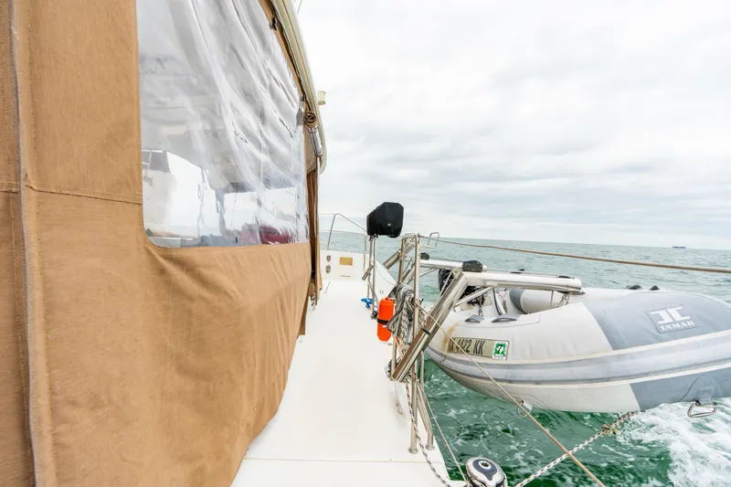 Slide: The Image of 2013 Lagoon 450 yacht with dinghy on open sea, featuring tan canvas cover. - 48