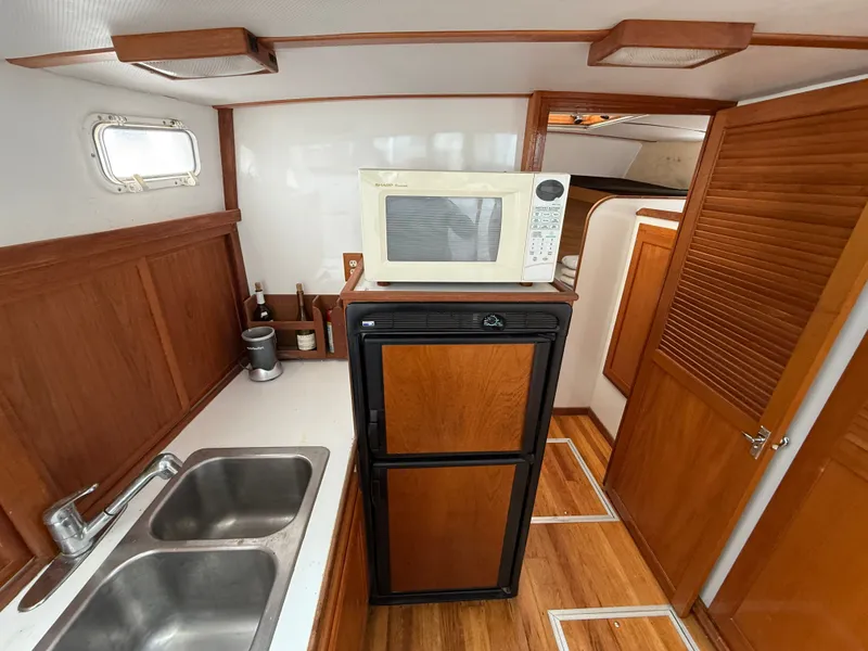 Slide: The Image of 1998 Wilbur 38 Downeast boat interior with kitchenette, featuring microwave, fridge, and double sink. - 21