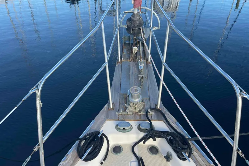 Slide: The Image of Bow of 1989 Island Packet 35 sailboat with ropes and winch, docked on calm water. - 14