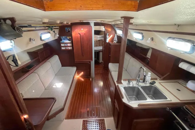 Slide: The Image of 1989 Island Packet 35 sailboat interior with wood finish, cozy seating, and kitchen area. - 15