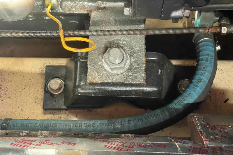 Slide: The Image of Engine component of a 1989 Island Packet 35 sailboat, featuring exhaust hose and mounting bolts. - 49