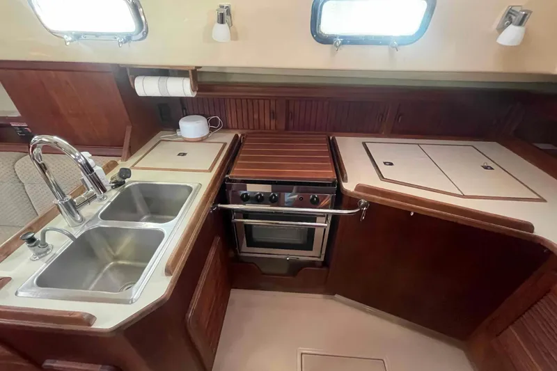 Slide: The Image of 1989 Island Packet 35 yacht kitchen with dual sinks, stove, and wooden cabinetry. - 5