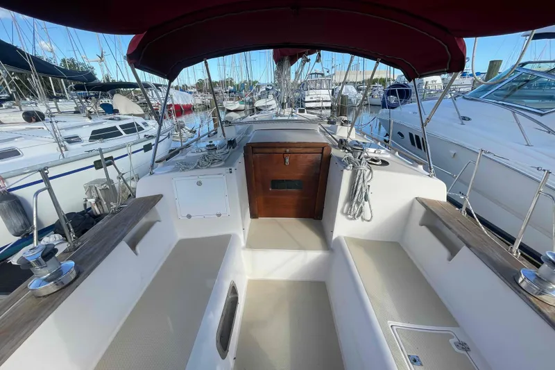 Slide: The Image of 1989 Island Packet 35 sailboat cockpit with red canopy, docked among other boats. - 60