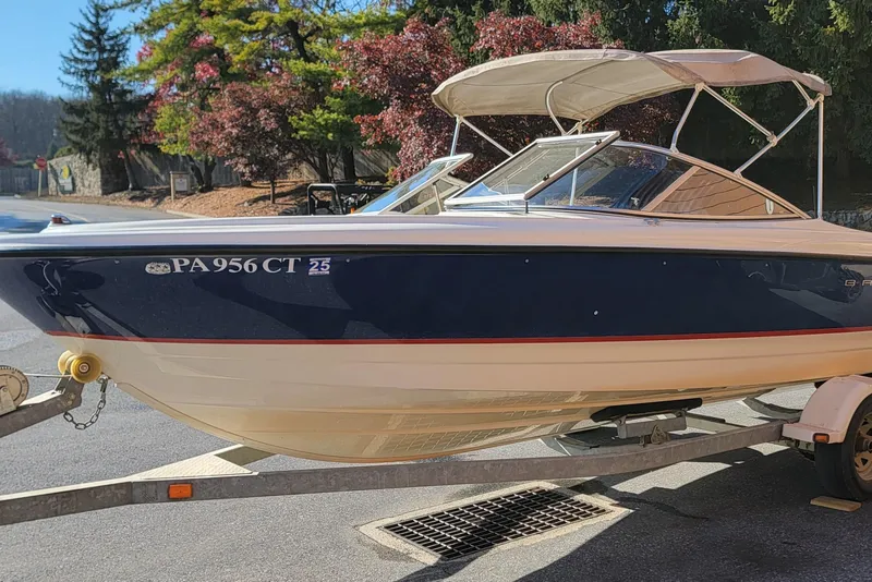 Slide: The Image of 2004 Bayliner 215 Classic boat on trailer, parked outdoors with trees in background. - 2