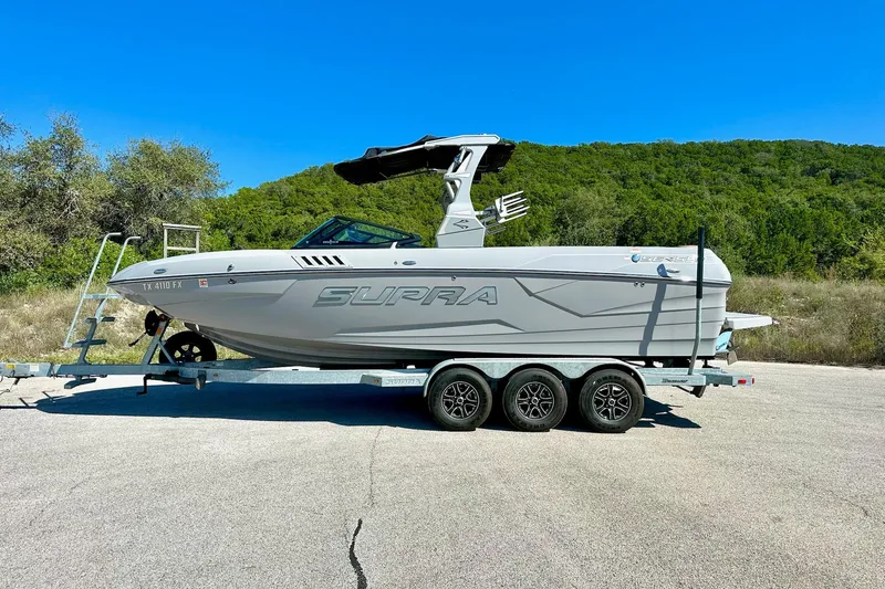 Slide: The Image of 2020 Supra SE550 boat on trailer, parked outdoors with green hills in background. - 10