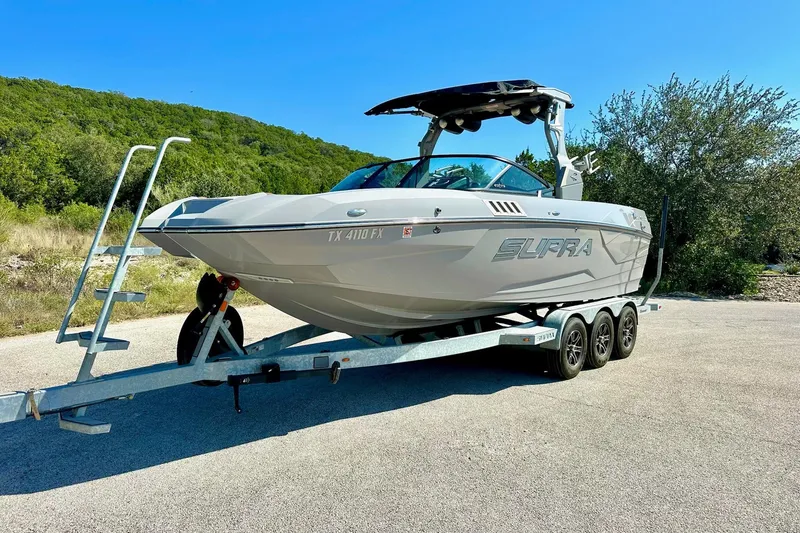 Slide: The Image of 2020 Supra SE550 boat on trailer, parked outdoors with lush greenery background. - 9