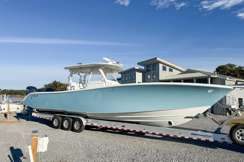 Slide: The Image of 2012 Yellowfin 39 Offshore boat on trailer, parked near modern buildings under clear blue sky. - 2