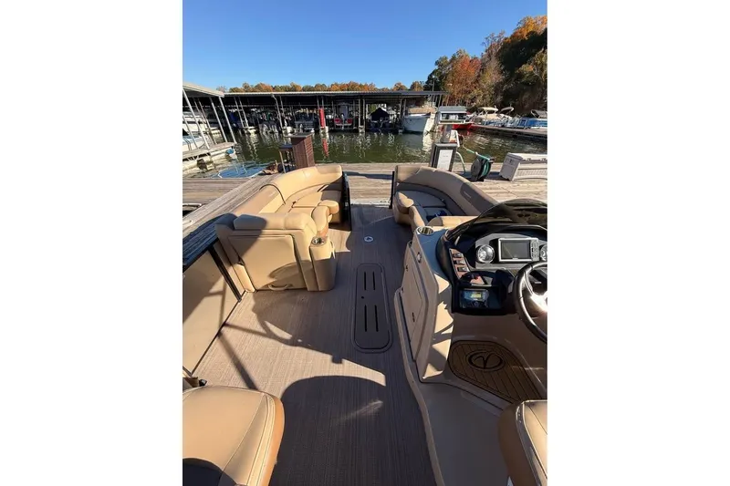 Slide: The Image of 2023 Veranda Relax VR22RC pontoon boat interior at marina, featuring tan seating and helm. - 7