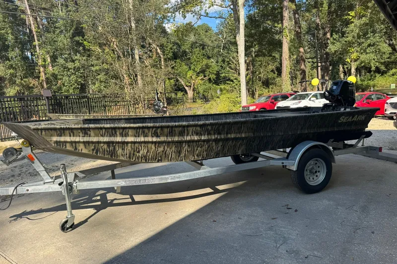 Slide: The Image of 2025 SeaArk 1648 MV Special boat on trailer, parked outdoors with trees in background. - 6