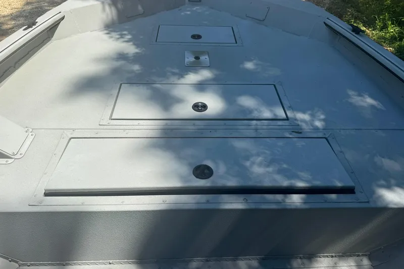 Slide: The Image of 2024 SeaArk Shadow 20 boat deck with storage compartments, shaded by trees. - 18