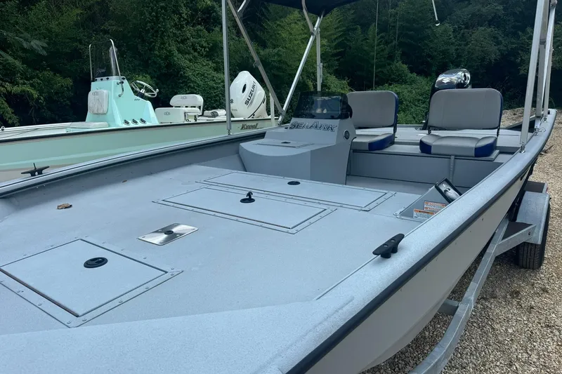 Slide: The Image of 2024 SeaArk Shadow 20 boat with spacious deck and seating, parked on gravel. - 28