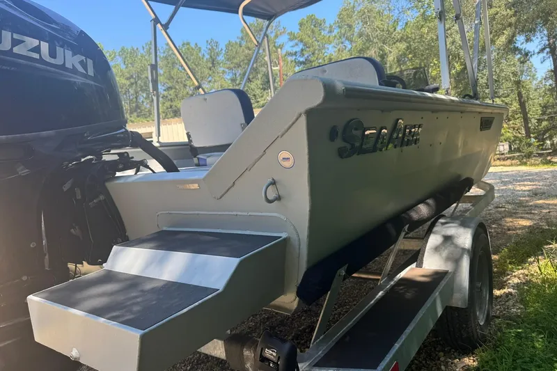 Slide: The Image of 2024 SeaArk Shadow 20 boat on trailer with Suzuki outboard motor in wooded area. - 7