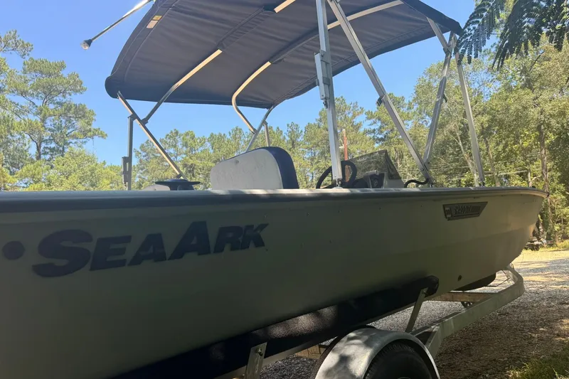 Slide: The Image of 2024 SeaArk Shadow 20 boat with canopy, parked on a trailer in a wooded area. - 9