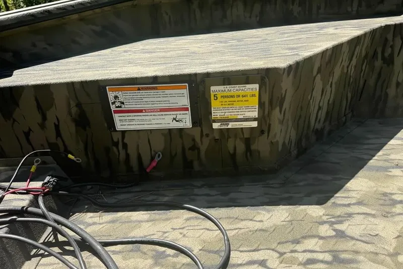 Slide: The Image of 2025 SeaArk 1752 Slayer Pro boat interior with capacity warning labels and camouflage design. - 13