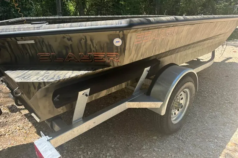 Slide: The Image of 2025 SeaArk 1752 Slayer Pro boat on trailer, camo design, parked outdoors. - 8