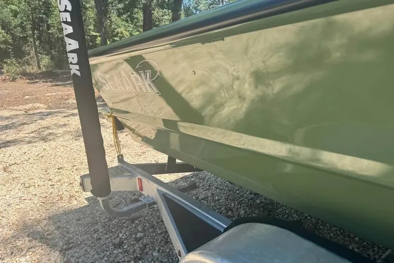 Slide: The Image of 2026 SeaArk 2672 MV boat on trailer, parked on gravel, surrounded by trees. - 7