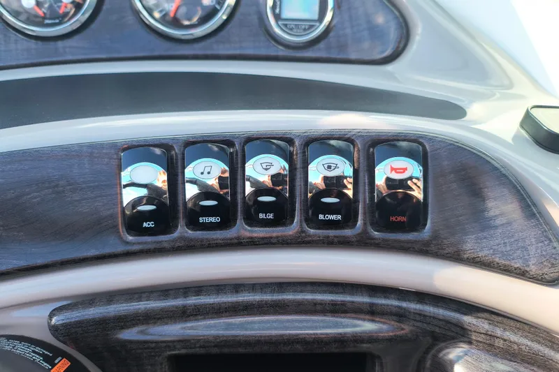 Slide: The Image of Dashboard controls of a 2018 Rinker QX23 BR boat, featuring accessory, stereo, bilge, blower, and horn switches. - 16