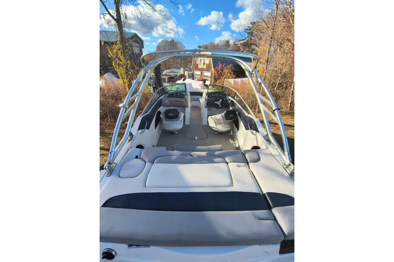 Slide: The Image of 2018 Rinker QX23 BR boat interior with seating and steering wheel, parked outdoors. - 27