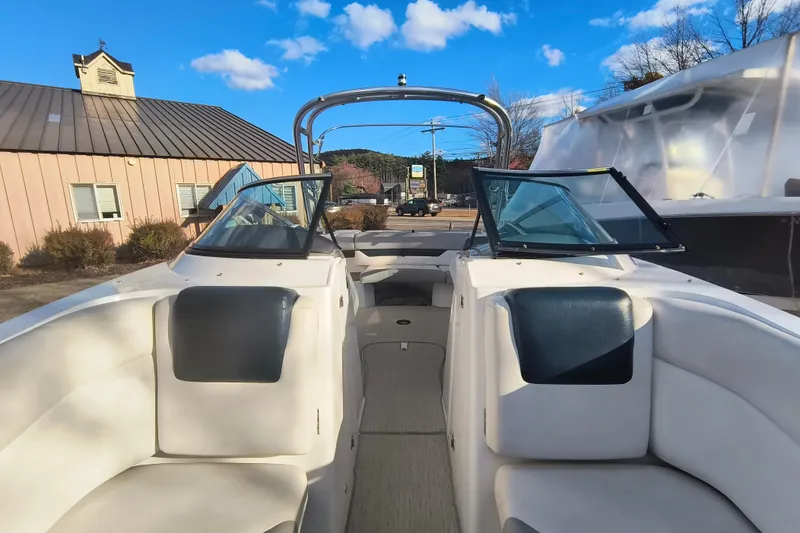 Slide: The Image of 2018 Rinker QX23 BR boat interior with open windshield, parked outdoors under blue sky. - 5