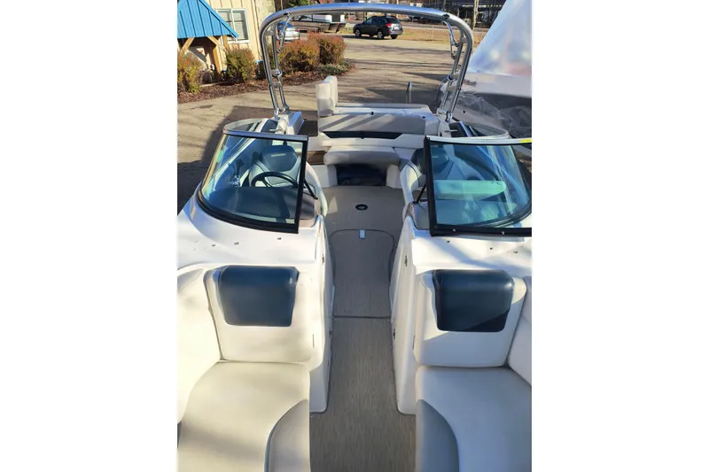 Slide: The Image of 2018 Rinker QX23 BR boat interior with seating and windshield, parked outdoors. - 6