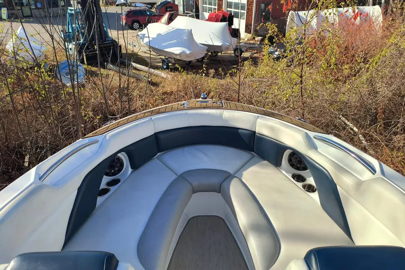 Slide: The Image of 2018 Rinker QX23 BR boat interior with cushioned seating and cup holders, parked outdoors. - 7