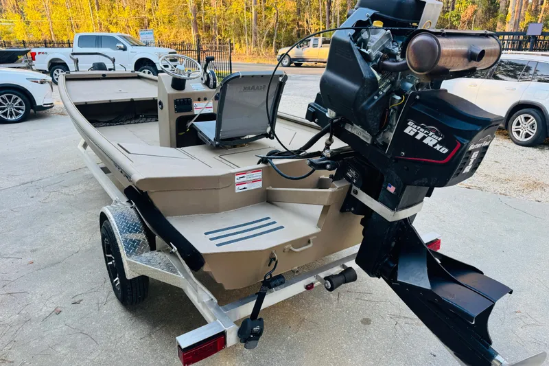 Slide: The Image of 2025 SeaArk Mud Runner 180 boat with motor, parked on a trailer in a driveway. - 15