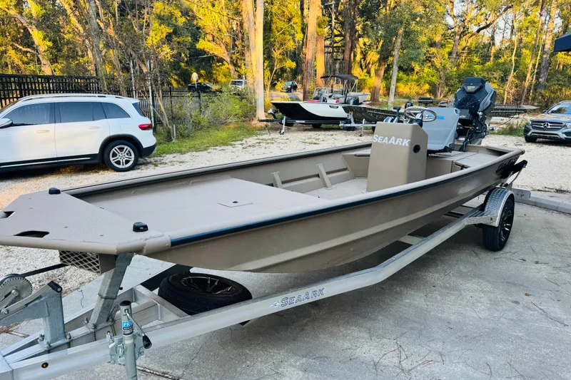 Slide: The Image of 2025 SeaArk Mud Runner 180 boat on trailer, parked outdoors with trees in background. - 16