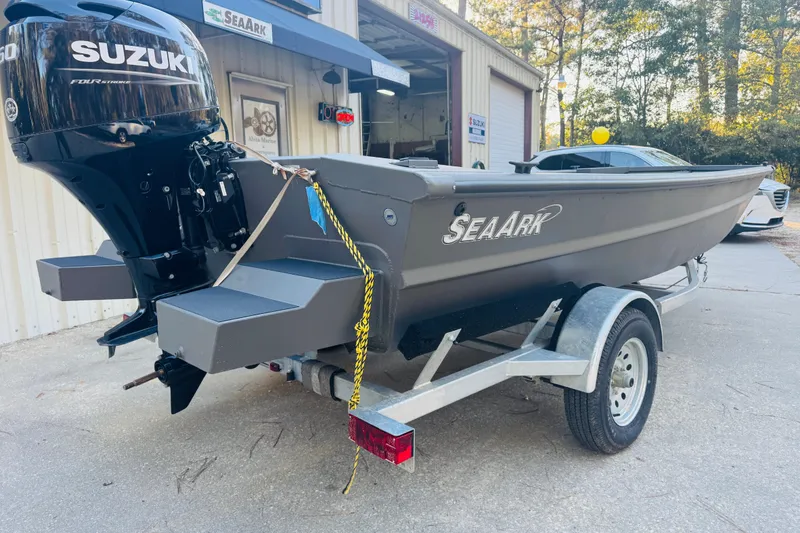 Slide: The Image of 2025 SeaArk 1660 MVT boat on trailer with Suzuki outboard motor, parked outside. - 7