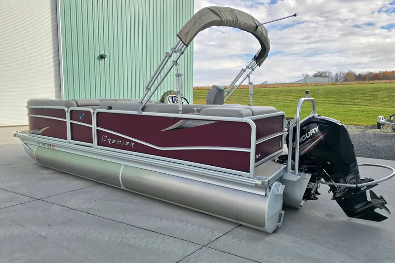 Slide: The Image of 2017 Premier 220 SunSation pontoon boat with outboard motor, parked near a green building. - 2