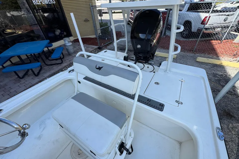 Slide: The Image of 2023 Mako 18 LTS boat interior with seating and motor, parked near a blue picnic table. - 15