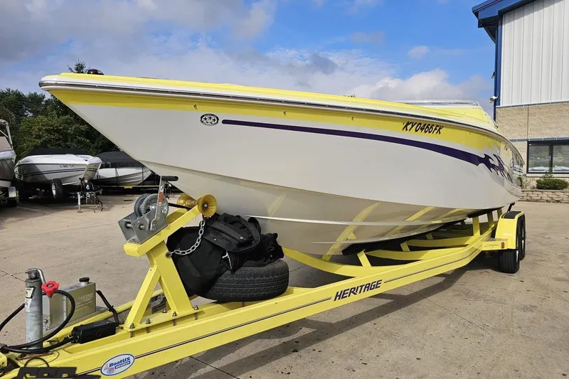 Slide: The Image of 2005 Baja 25 Outlaw speedboat on yellow trailer, parked outdoors near other boats. - 28