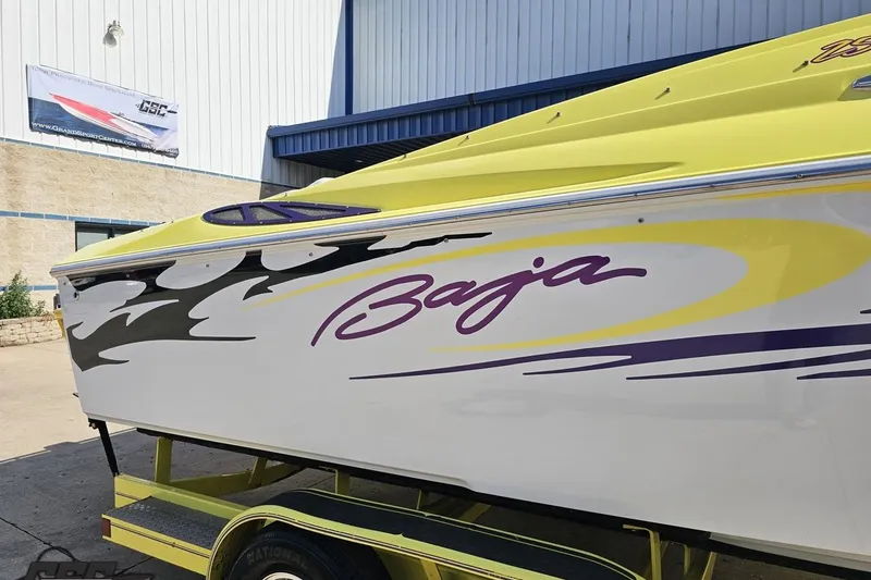 Slide: The Image of 2005 Baja 25 Outlaw boat with vibrant yellow and purple graphics, parked outside a building. - 7