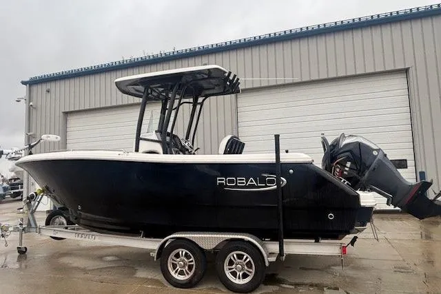 Slide: The Image of 2021 Robalo R230 Center Console boat on trailer, black hull, parked outside a garage. - 4
