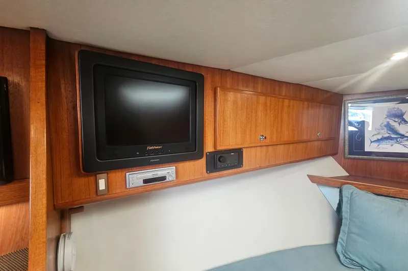 Slide: The Image of Interior of 2003 Topaz 32 Express boat with TV, wooden cabinets, and blue cushions. - 55