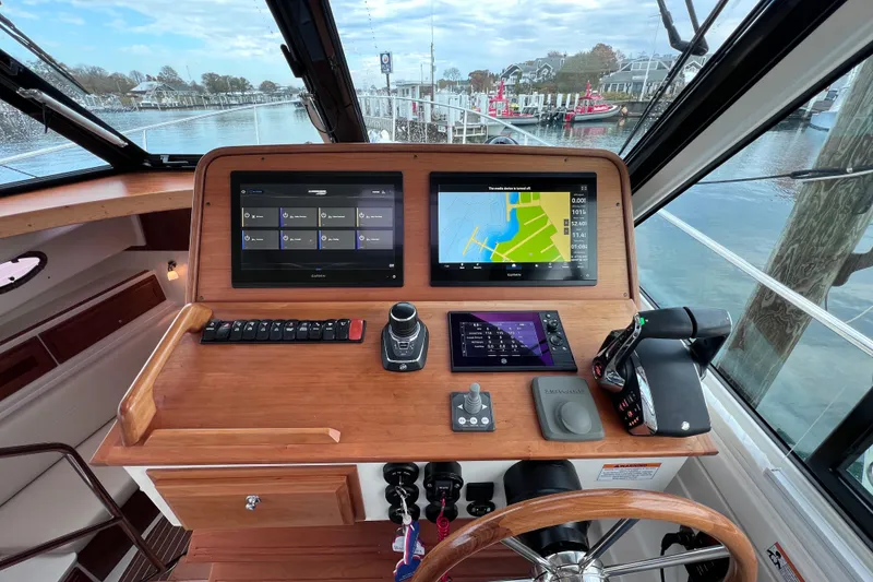 Slide: The Image of 2024 Back Cove 39O helm with navigation screens and controls, docked by the water. - 17