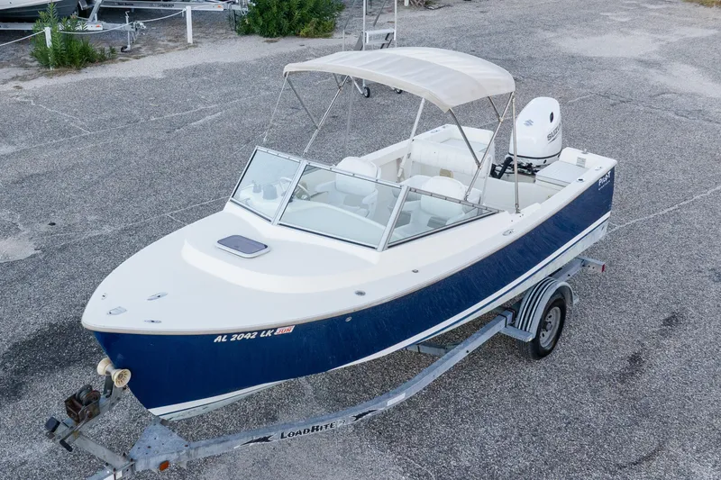 Slide: The Image of 2004 Hoby Pilot 19 boat on trailer, blue and white design, parked on gravel. - 2