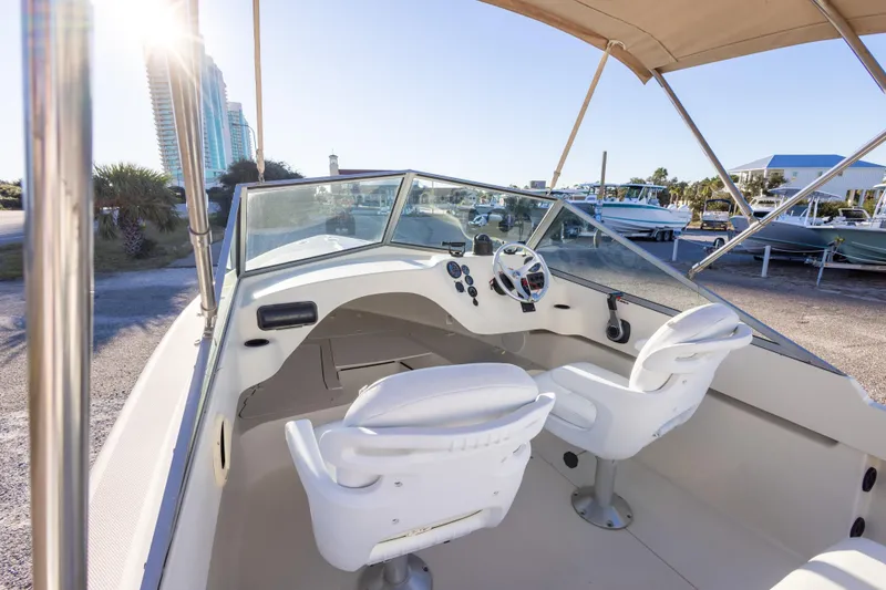 Slide: The Image of 2004 Hoby Pilot 19 boat interior with steering wheel and seats, docked under sunny sky. - 22