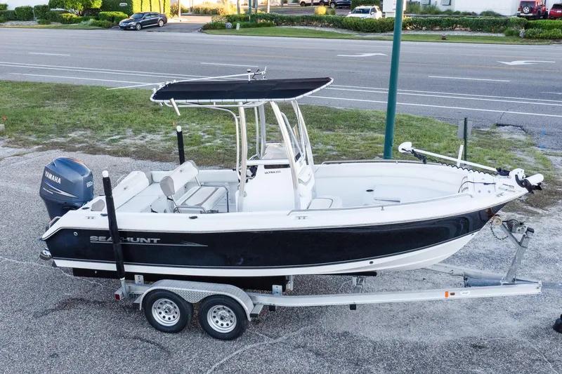 The Image of 2010 Sea Hunt Ultra 210 boat on trailer with Yamaha engine, parked near road. - 0