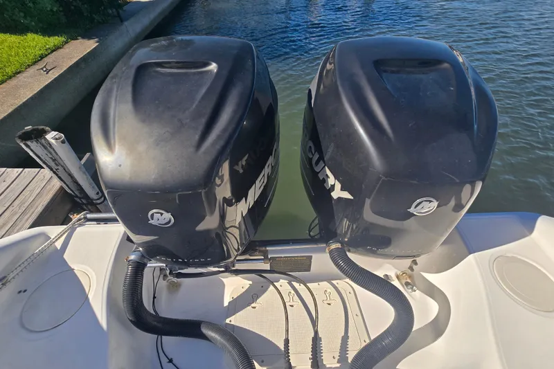 Slide: The Image of Twin Mercury outboard engines on a 2004 Boston Whaler 270 Outrage boat by the water. - 25