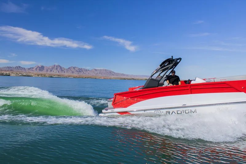 Slide: The Image of 2024 Paradigm Damascus 296 Surf boat cruising on a lake with mountains in the background. - 12